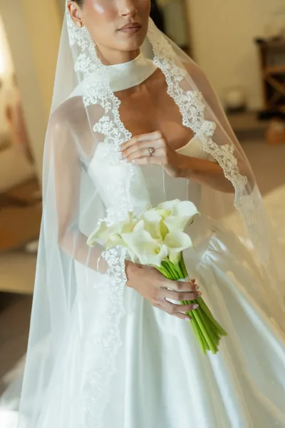 Bridal portrait with a lace mantilla veil as the bride holds a calla lily bouquet in soft natural light against warm neutral walls