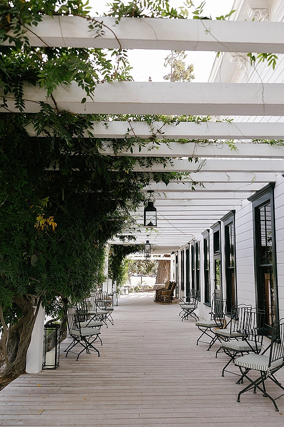 Outdoor walkway decor with a white pergola walkway, hanging lanterns and climbing vines over patio chairs and bistro tables on a wooden deck