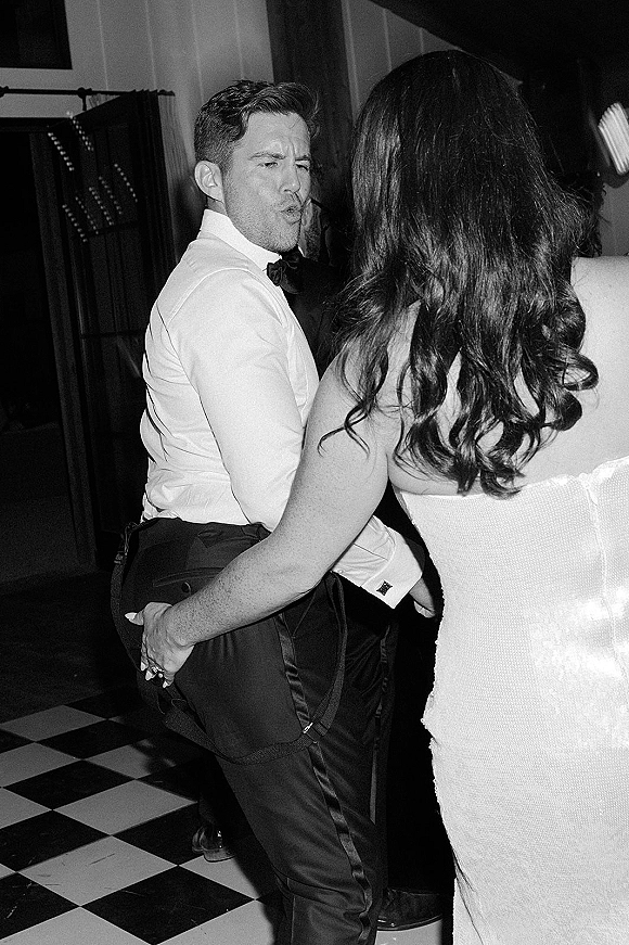 Wedding reception dancing in a black and white wedding photo, bride in strapless dress holding groom on a checkered dance floor under drapery