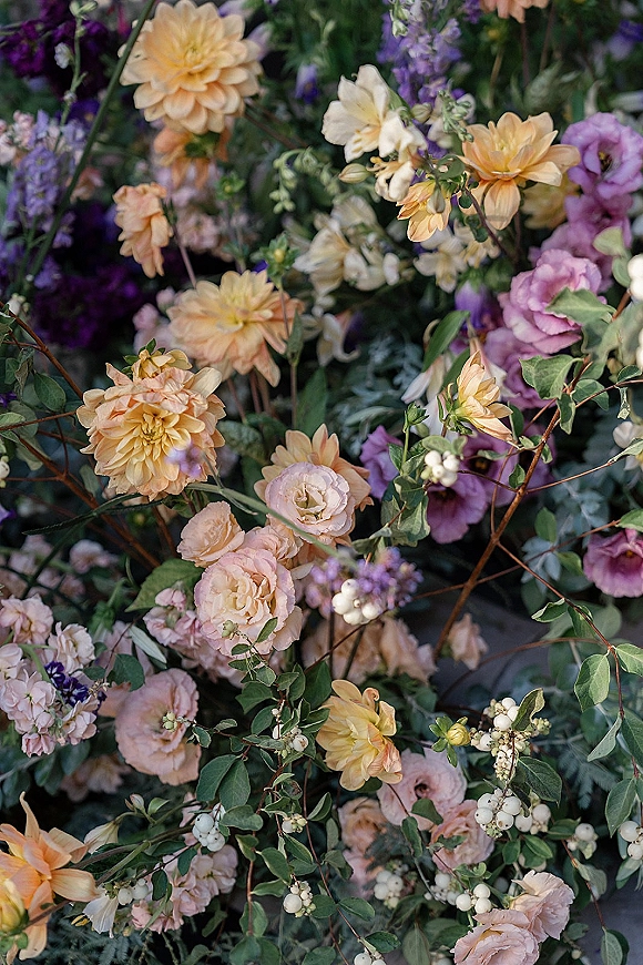 Wedding flowers featuring dahlia wedding flowers in peach and purple with roses, lisianthus, lavender, greenery, and white berries in lush foliage