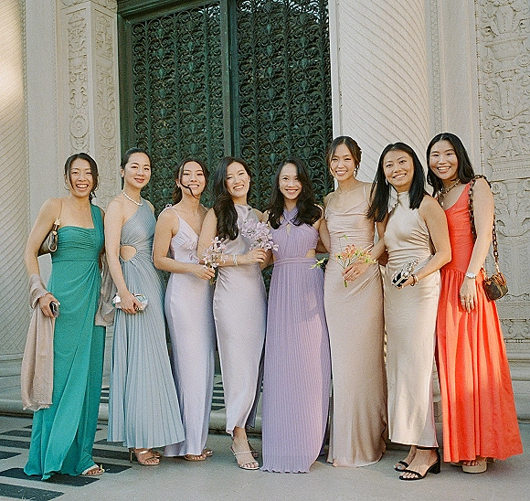 Bridesmaid group photo of bridesmaids posing together in mismatched dresses, holding small bouquets before ornate iron doors and columns