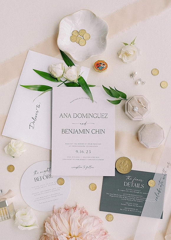 Invitation suite wedding invitation flat lay with wax-sealed envelope, white roses, greenery, ring box, and pearl earrings on neutral fabric