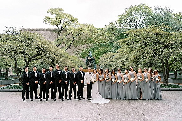 Wedding party portrait with bride and groom with bridal party, bridesmaids holding white bouquets on a stone walkway by a garden fountain