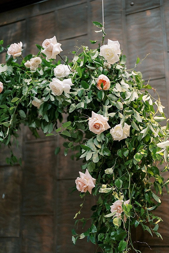 Wedding floral arch with roses and hanging greenery framing wood-paneled doors, lush foliage garland in an asymmetrical design