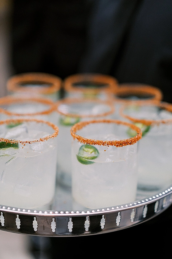 Wedding cocktails in clear tumblers with salt-rimmed signature wedding cocktail, lime wedges and ice on a silver tray against dark drapery