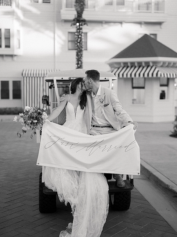 Wedding kiss portrait of bride and groom kissing in a golf cart with a just married banner, palm tree and striped awnings behind