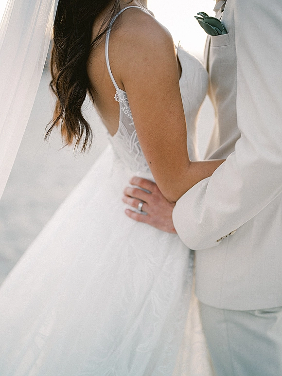 Wedding couple portrait of bride and groom embrace, her lace bodice and veil in soft outdoor light against open sky