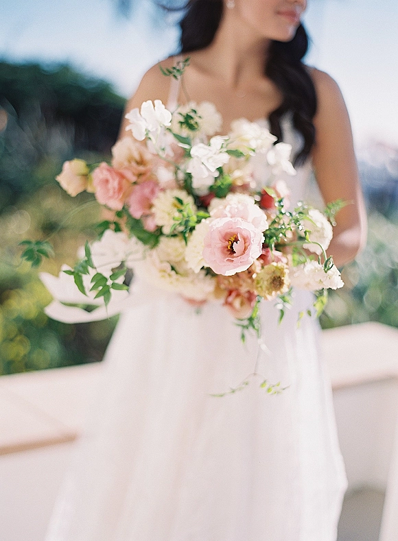 Bridal bouquet of blush wedding bouquet roses and ivory blooms with greenery, held by a bride in a simple gown on an outdoor railing terrace