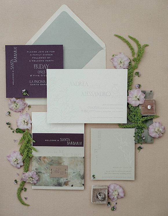 Wedding invitation suite with modern invitation suite accents, envelopes and RSVP cards, wax seal, twine, rings, and pink flowers on neutral paper backdrop