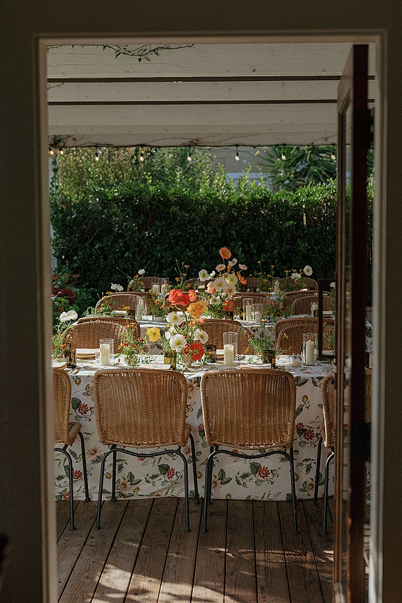 Reception tablescape with outdoor reception table styling, wildflower centerpieces, floral tablecloth, candles and string lights under pergola beams