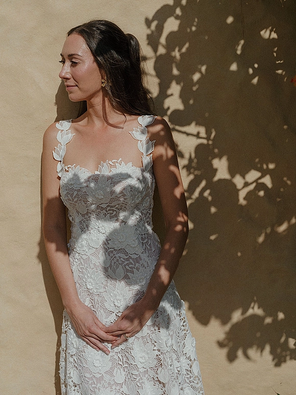 Bridal portrait in a lace wedding dress, bride in side profile leaning on a stucco wall with leaf shadows in natural light