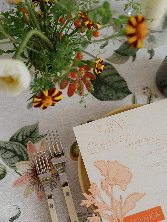 Wedding menu card with floral illustration and wedding menu design on dinner plate, set with flatware, glassware, and flower centerpiece