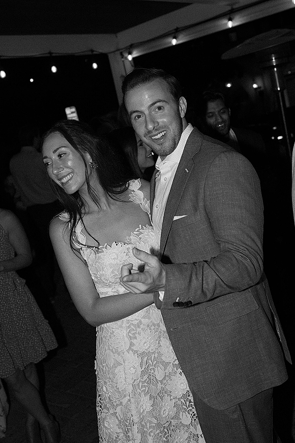 Wedding reception dancing as bride in lace dress and groom in suit share a close first dance under string lights in a tented night reception