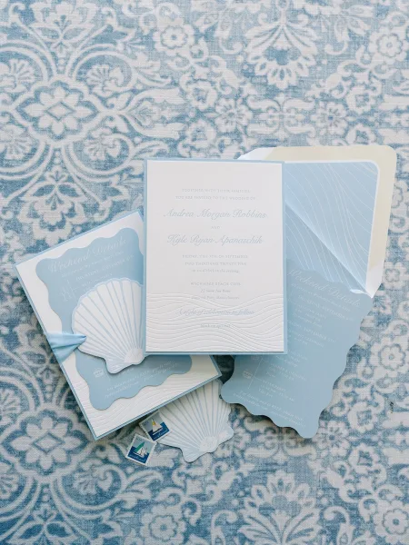 Invitation suite of blue wedding invitations with embossed cards, scallop edges, ribbon bow, and sailboat stamps on blue patterned fabric