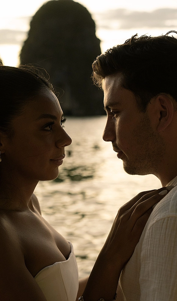 Couple portrait of bride and groom close up, forehead to forehead at sunset by ocean water and rocky cliff, bride in strapless dress