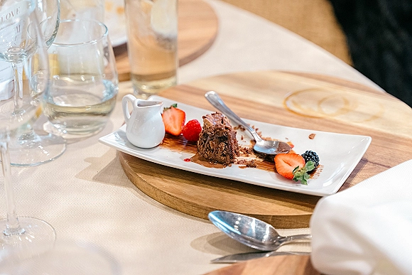 Wedding dessert plate with chocolate cake and fresh berries on a rectangular white plate, dessert sauce, at a reception table with blurred guests