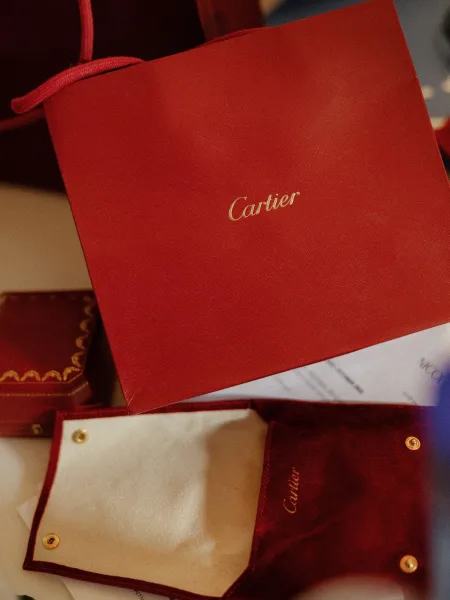Wedding invitations in a red folder with gold foil lettering, cards and envelope arranged on a tabletop with scattered paper