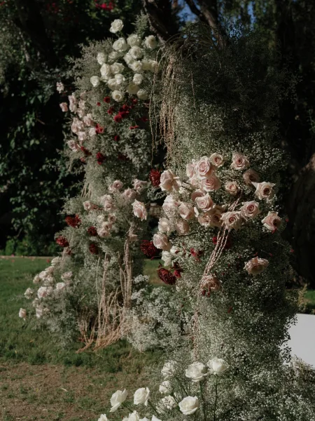 Ceremony aisle decor with aisle floral arrangements of roses and baby's breath, grounded with greenery and dried branches on a garden lawn