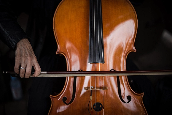 Wedding cello music close-up of a cellist at wedding, bow drawn across strings with ringed hand and black suit against dark backdrop