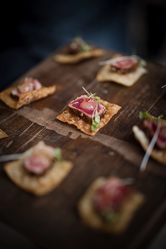 Wedding passed appetizers with cocktail hour appetizers of seared tuna on crackers, topped with microgreens on a wood serving board against dark backdrop