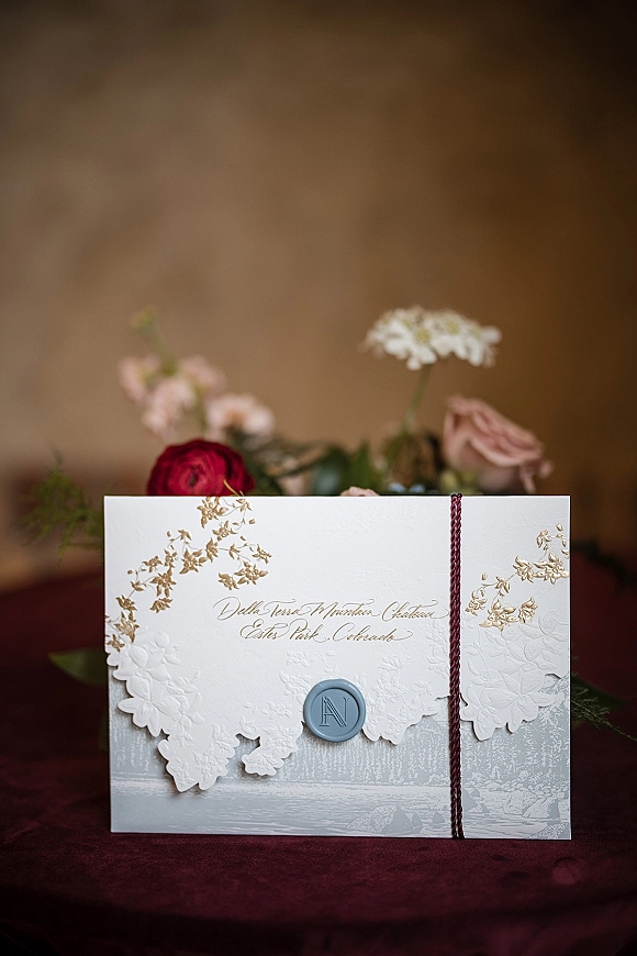 Wedding invitation suite with letterpress wedding invitation details, gold foil lettering, wax monogram seal, and burgundy string on fabric backdrop