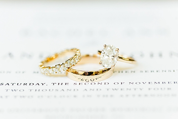 Wedding rings stacked with an oval diamond engagement ring and diamond band on a printed invitation over white paper background