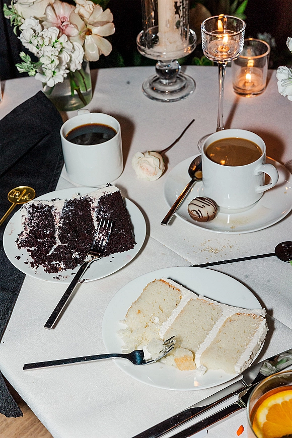 Wedding dessert table with wedding cake slices on plates beside coffee cups and candlelit glass votives in dim reception lighting