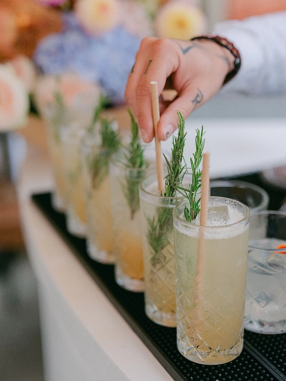 Signature cocktails on a cocktail tray, wedding signature drink highball glasses with ice and a rosemary sprig garnish on a bar top