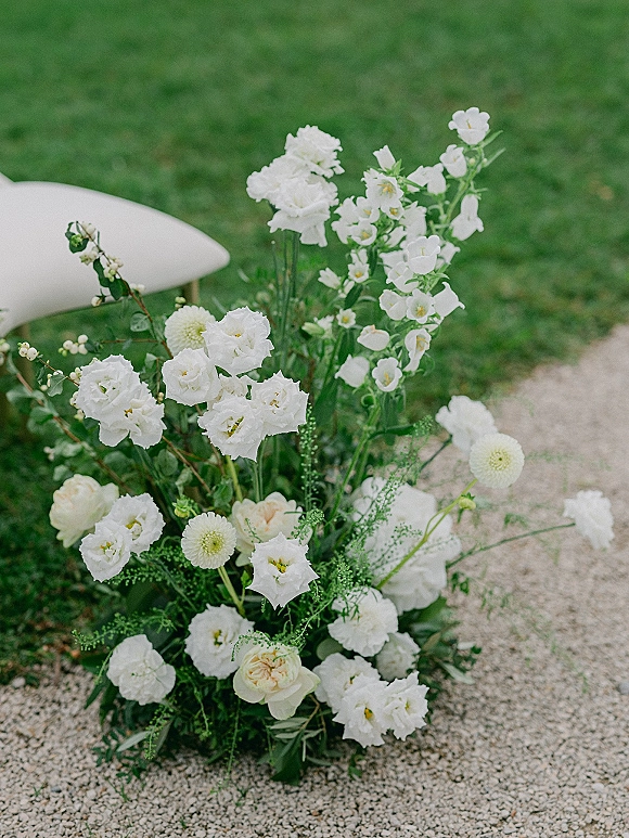 Ceremony aisle flowers in an aisle ground floral arrangement of white blooms and greenery along a gravel path on a grass lawn
