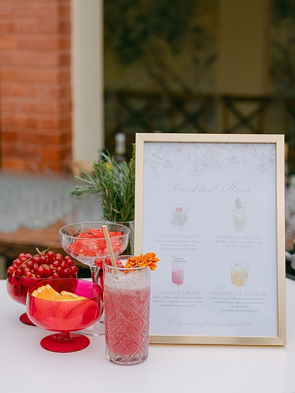 Cocktail menu sign in a frame with calligraphy wedding bar signage beside glassware, citrus bowls, and rosemary on a white tablecloth
