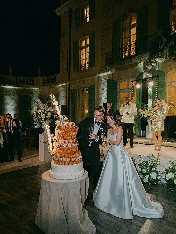 Wedding cake cutting as bride and groom slice a croquembouche wedding cake with sparklers, champagne flutes, in a night courtyard estate reception