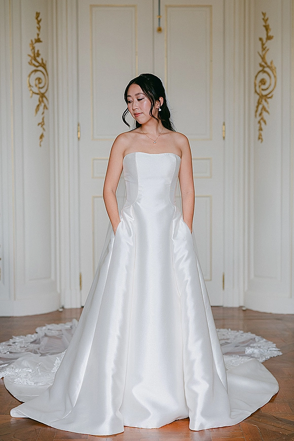 Bridal portrait of a bride in a strapless wedding dress with lace train, pearl earrings and necklace before ornate white doors
