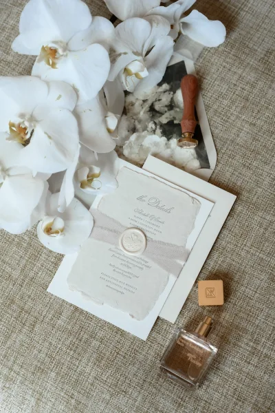 Wedding invitation suite with deckle edge invitations accented by orchids on linen fabric, arranged in a soft, airy flat lay.