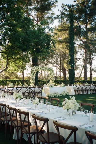 Outdoor reception decor with long banquet tables glowing under string lights, arranged in a symmetrical layout for an open-air wedding dinner