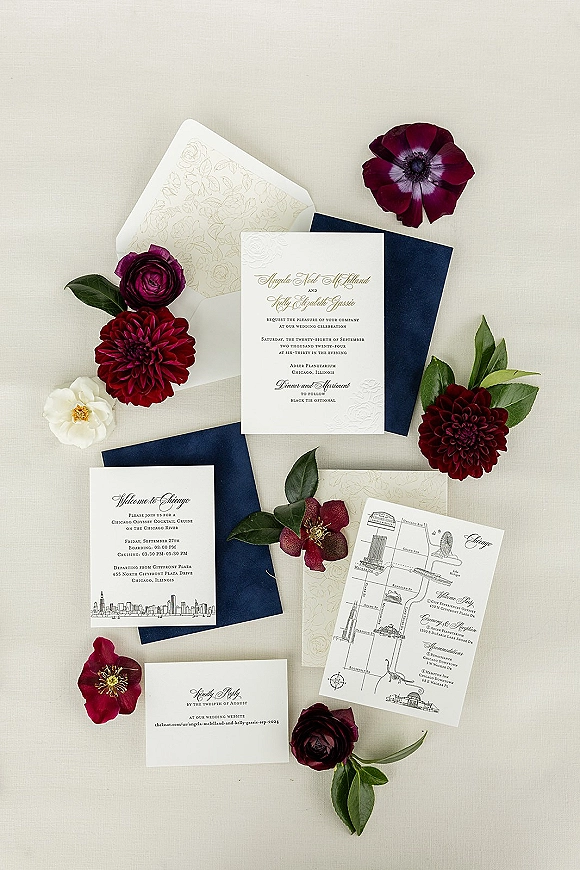 Wedding invitation suite with letterpress wedding invitations, navy envelopes and ivory cards accented by burgundy flowers on light fabric surface