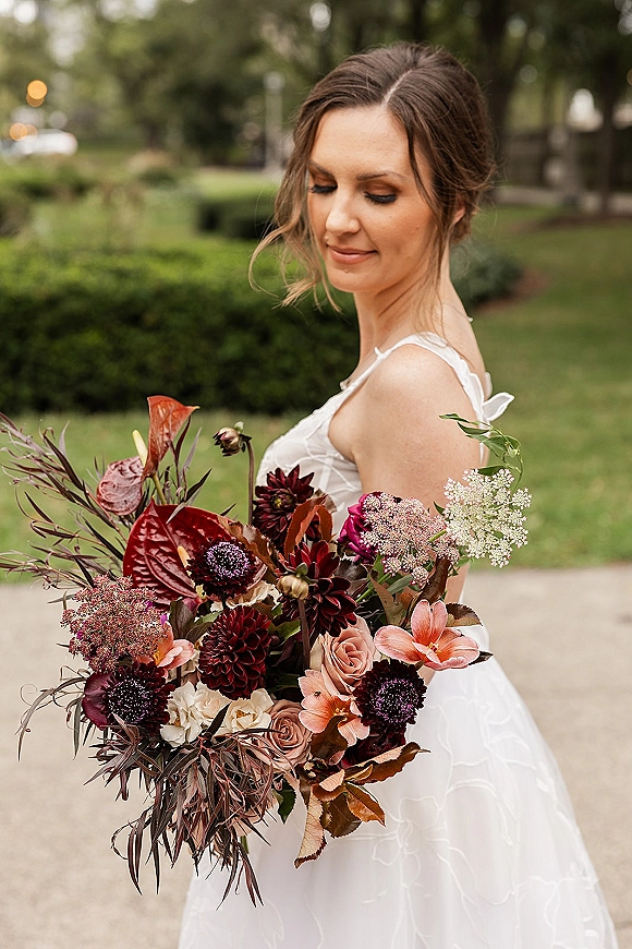Bridal portrait of a bride holding bouquet, looking down in a spaghetti strap white gown with rose and dahlia bouquet in a garden walkway
