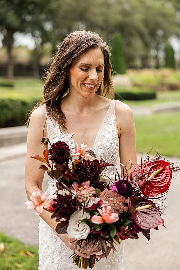 Bridal portrait of a bride holding bouquet with anthurium and dahlias, smiling and looking down in a garden walkway setting