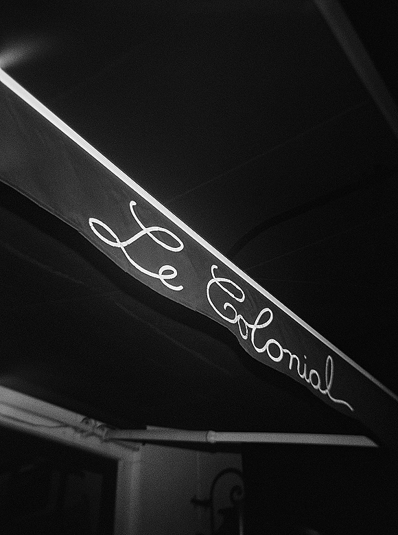 Wedding signage with calligraphy wedding sign lettering hanging from a metal bracket beneath dark ceiling beams, elegant black-and-white script