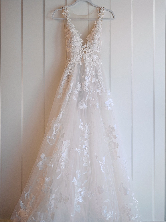 Wedding dress, lace wedding dress on a hanger with floral appliqué and sheer tulle skirt against a white paneled wall