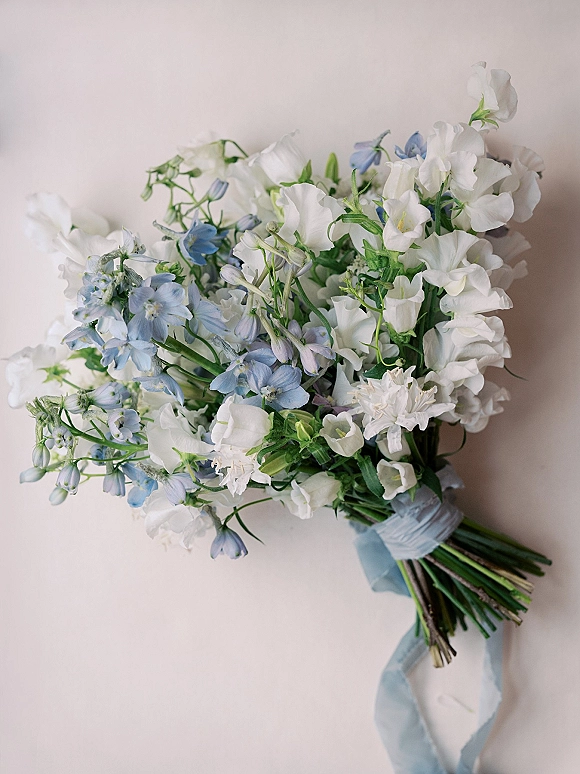 Bridal bouquet with white and blue bouquet blooms and airy greenery, wrapped in a light blue ribbon against a clean white backdrop