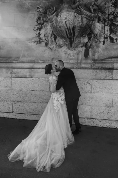 Wedding kiss portrait of bride and groom kissing in front of a stone wall, her lace dress with long tulle train and updo visible