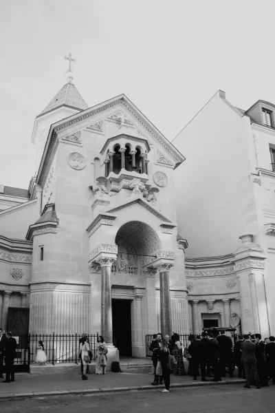 Church wedding exit with wedding guests gathered in suits and dresses beneath stone columns and a cross outside the city church facade