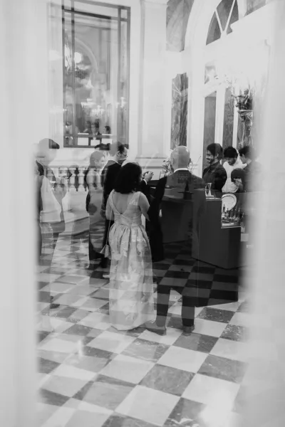 Wedding cocktail hour guests mingling beside a wedding bar setup with glassware on a checkered marble floor in a grand foyer with chandeliers