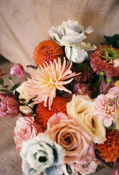 Bridal bouquet with colorful bridal bouquet blooms of dahlias, roses, zinnias and ranunculus, arranged with greenery on neutral fabric backdrop