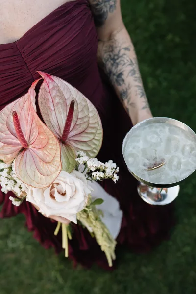 Bridesmaid bouquet with anthurium wedding bouquet and white roses, held by a tattooed bridesmaid in a burgundy dress on a green lawn