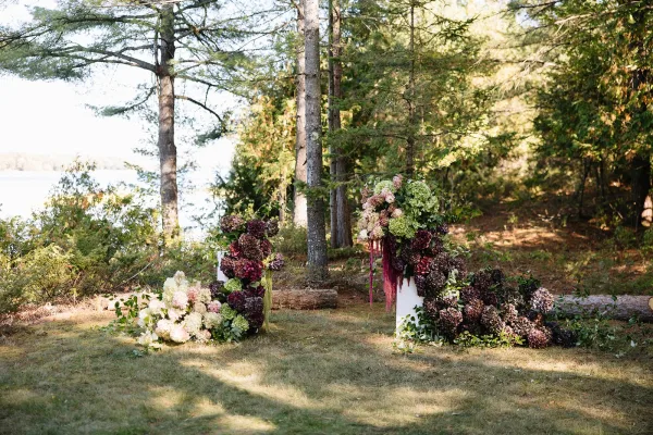 Wedding ceremony decor with outdoor wedding altar flowers on pedestal stands, hydrangeas and greenery, set on a forest lawn by a lake