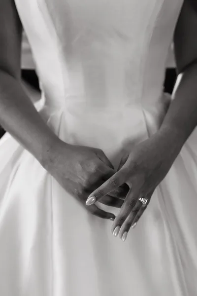 Bridal dress close-up of bride’s hands clasped on a strapless satin wedding dress bodice, showing emerald-cut ring in soft indoor light