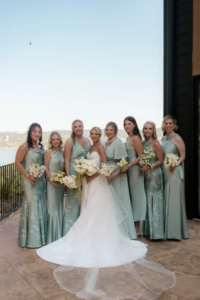 Bridesmaid group photo with bride with bridesmaids in mint dresses, holding white bouquets on a waterfront terrace with hills beyond