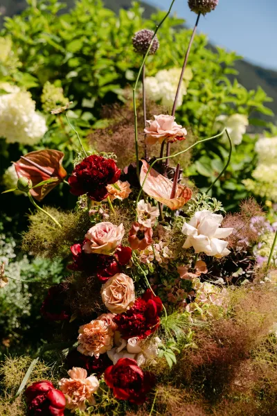 Wedding floral arrangement with ceremony arch flowers featuring roses, peonies, anthurium and greenery against garden foliage and mountains