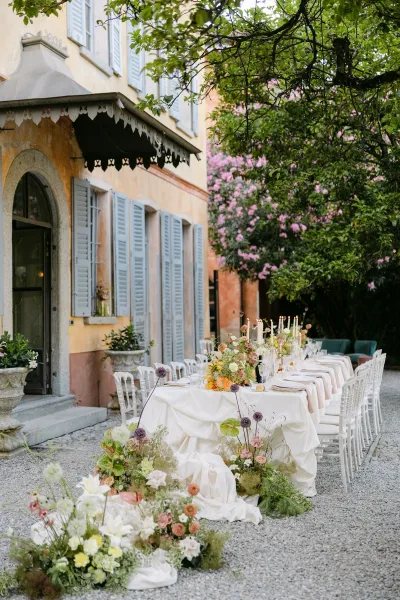 Reception tablescape with an outdoor wedding reception table, taper candles in clear glass candlesticks and floral runner in a villa courtyard